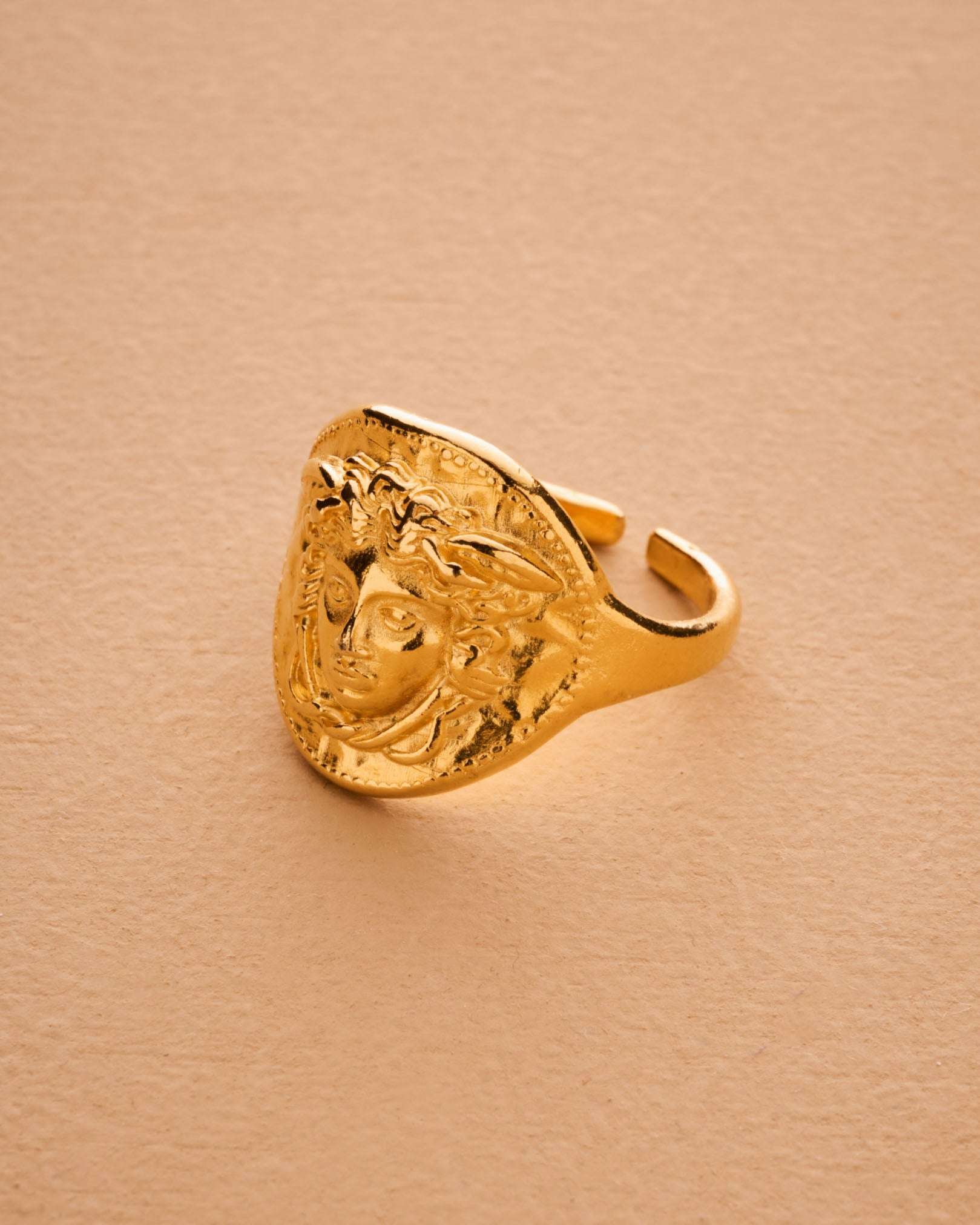 Gold ring with a face design on a beige background