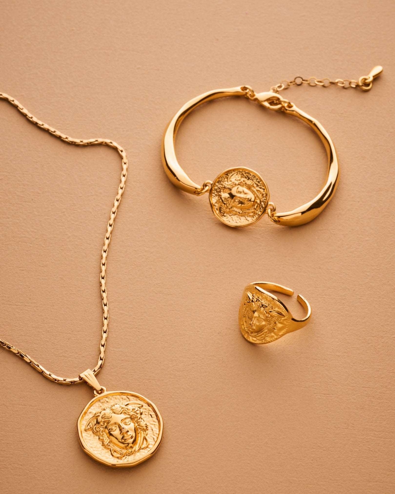 Gold necklace, bracelet, and ring set on a beige background