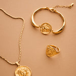 Gold necklace, bracelet, and ring set on a beige background