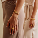 Two people holding hands with gold jewelry against a neutral background